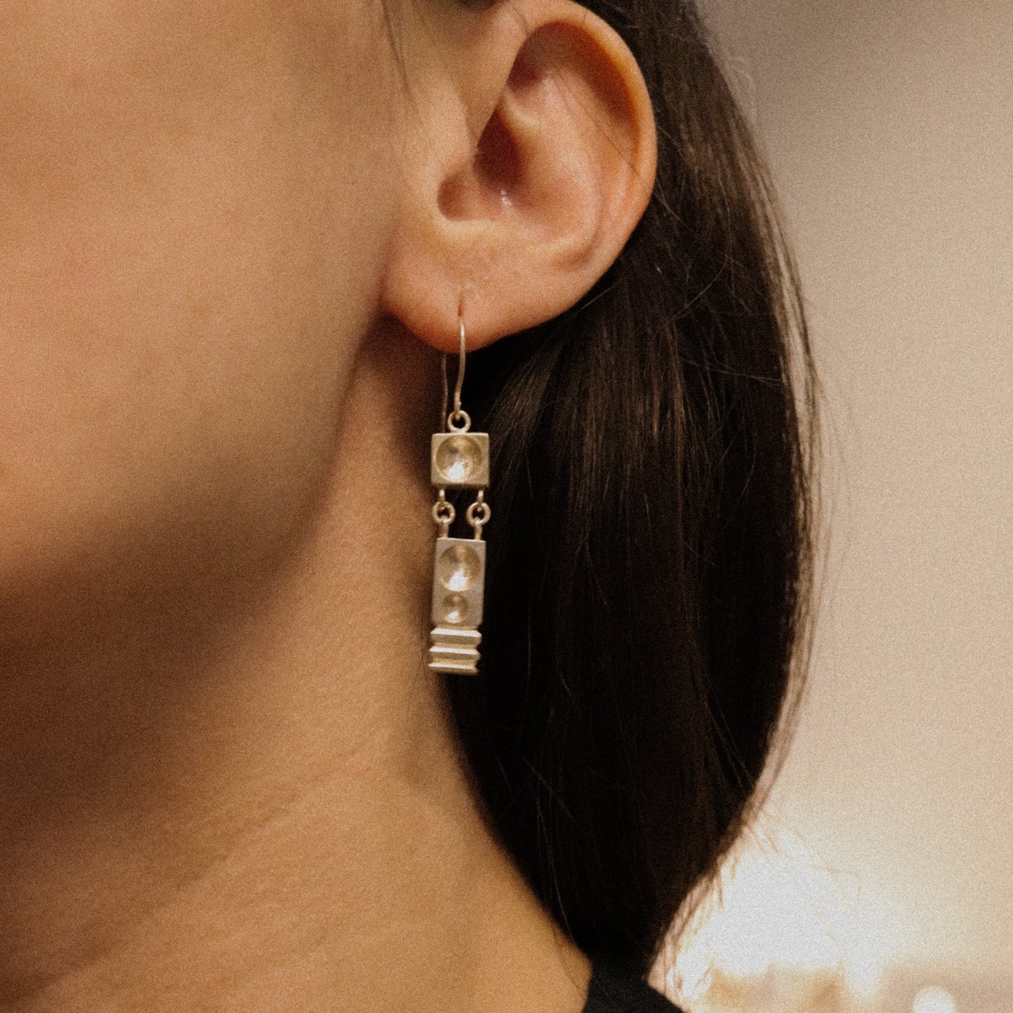 Close-up of an ear wearing a silver earring with a neutral background