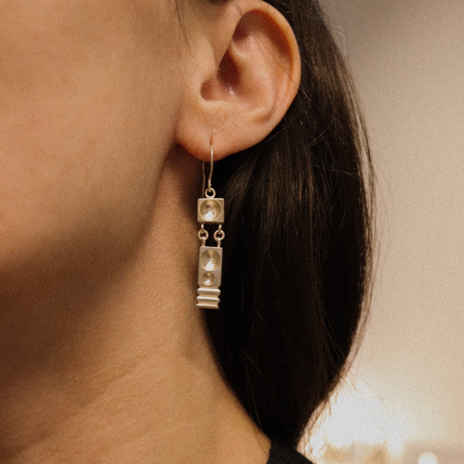 Close-up of an ear wearing a silver earring with a neutral background