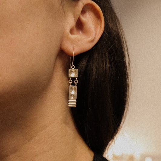 Close-up of an ear wearing a silver earring with a neutral background