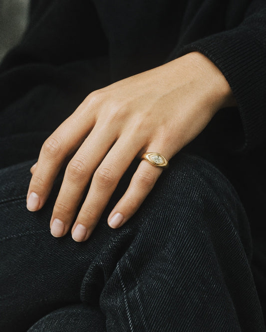 A close-up of a person's hand resting on dark denim, wearing a gold ring with a white oval stone.