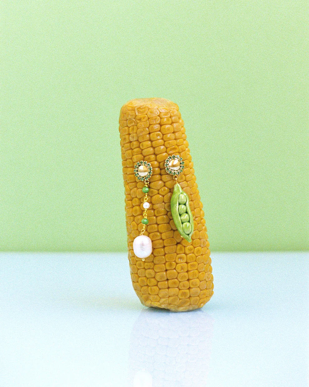 Corn on the cob with decorative earrings on a light green background
