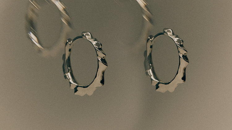 Pair of silver hoop earrings on a reflective surface with a blurred background
