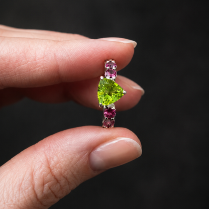 Jewelry with green gemstone held between fingers against a dark background