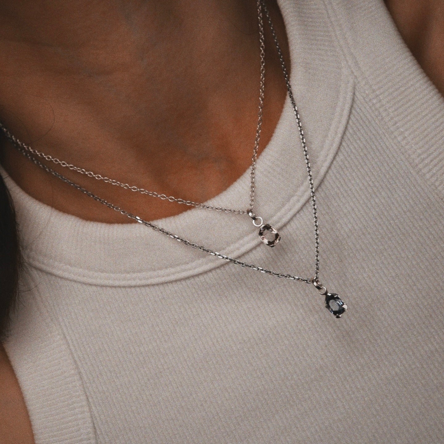 Close-up of a person wearing two silver necklaces with small pendants on a neutral background