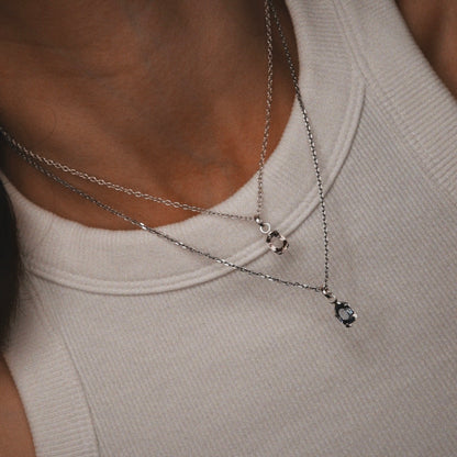 Close-up of a person wearing two silver necklaces with small pendants on a neutral background