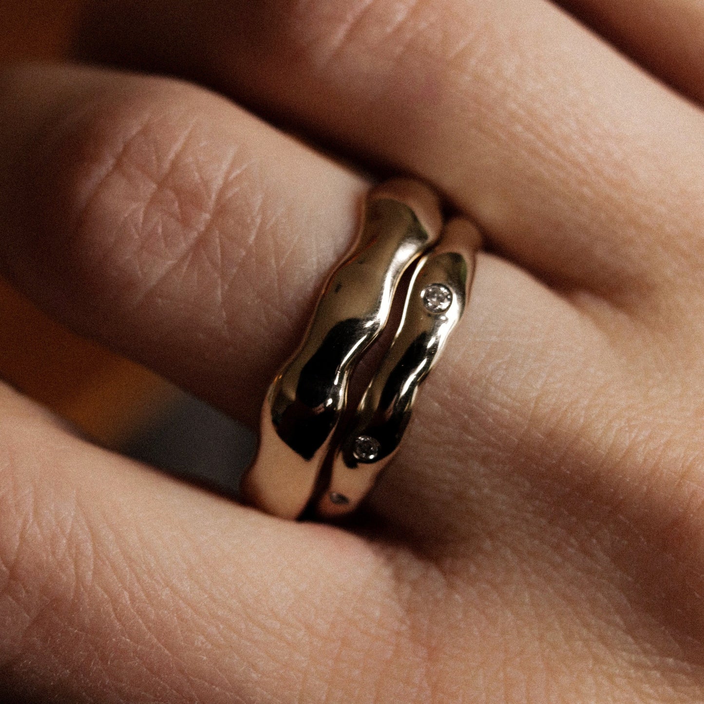 Close-up of a hand wearing a gold ring with a diamond on a blurred background