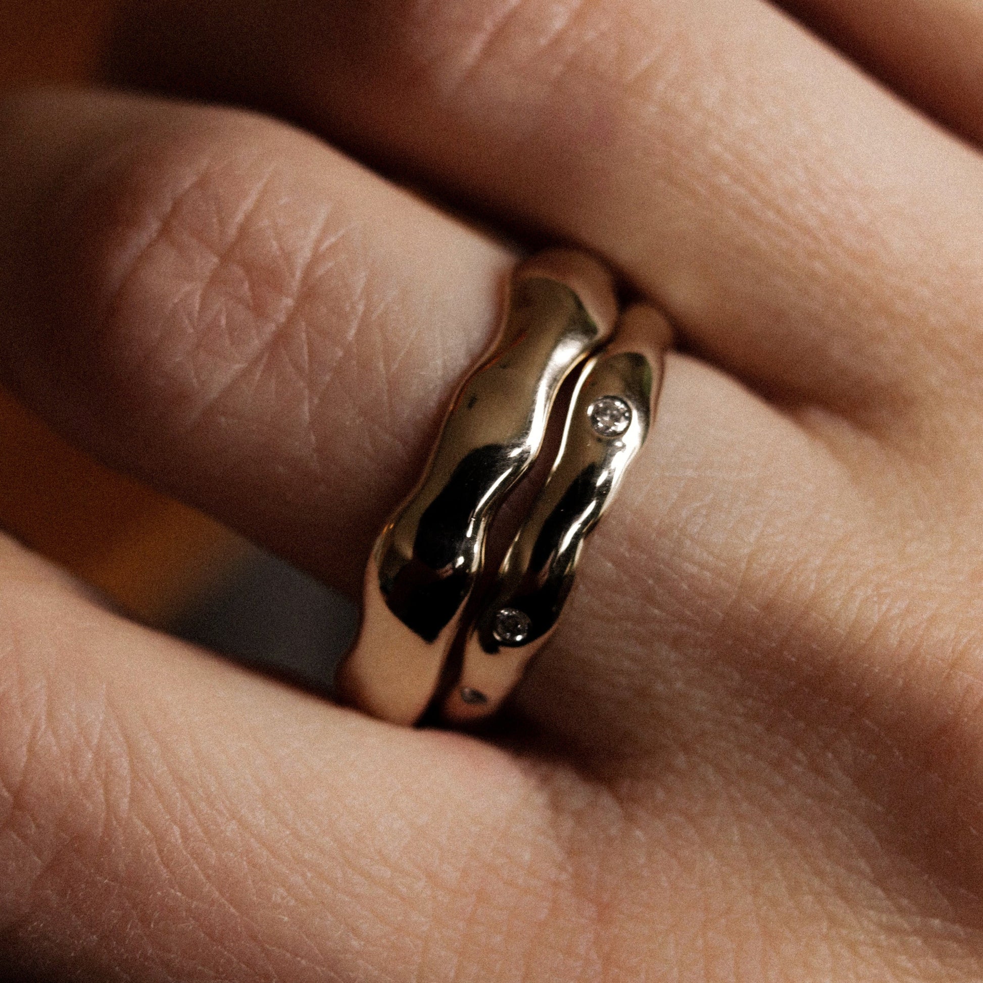 Close-up of a hand wearing a gold ring with a diamond on a blurred background