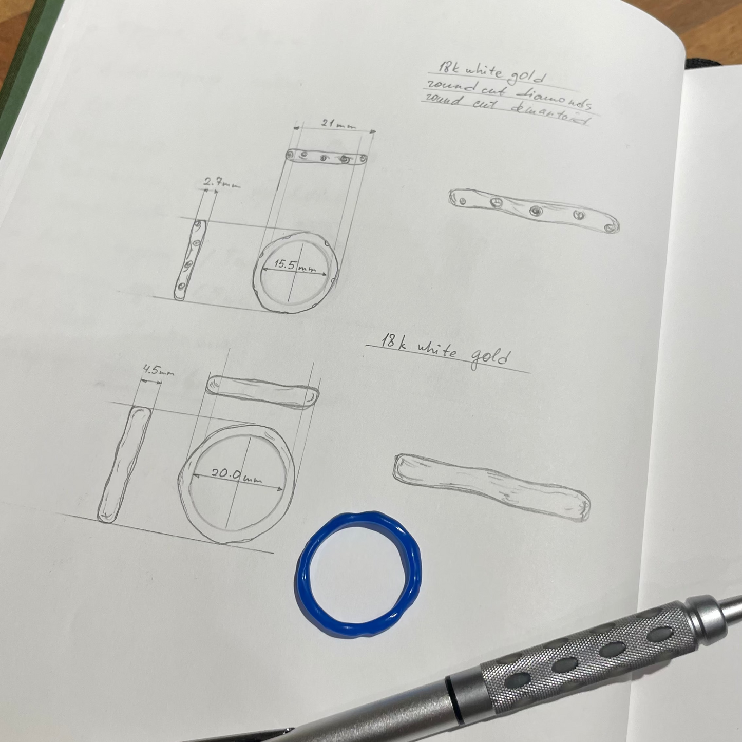 Open notebook with technical drawings and a pen on a wooden surface
