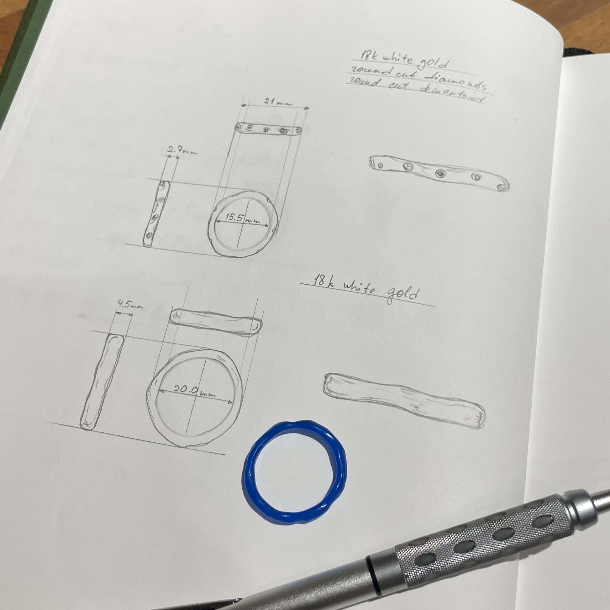 Open notebook with technical drawings and a pen on a wooden surface