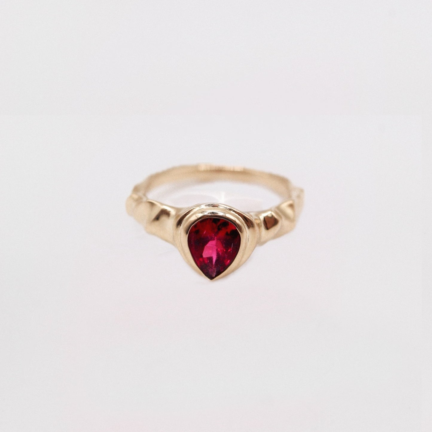 Gold ring with a heart-shaped red gemstone on a light gray background
