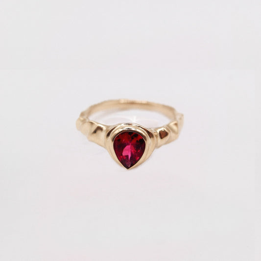 Gold ring with a heart-shaped red gemstone on a light gray background