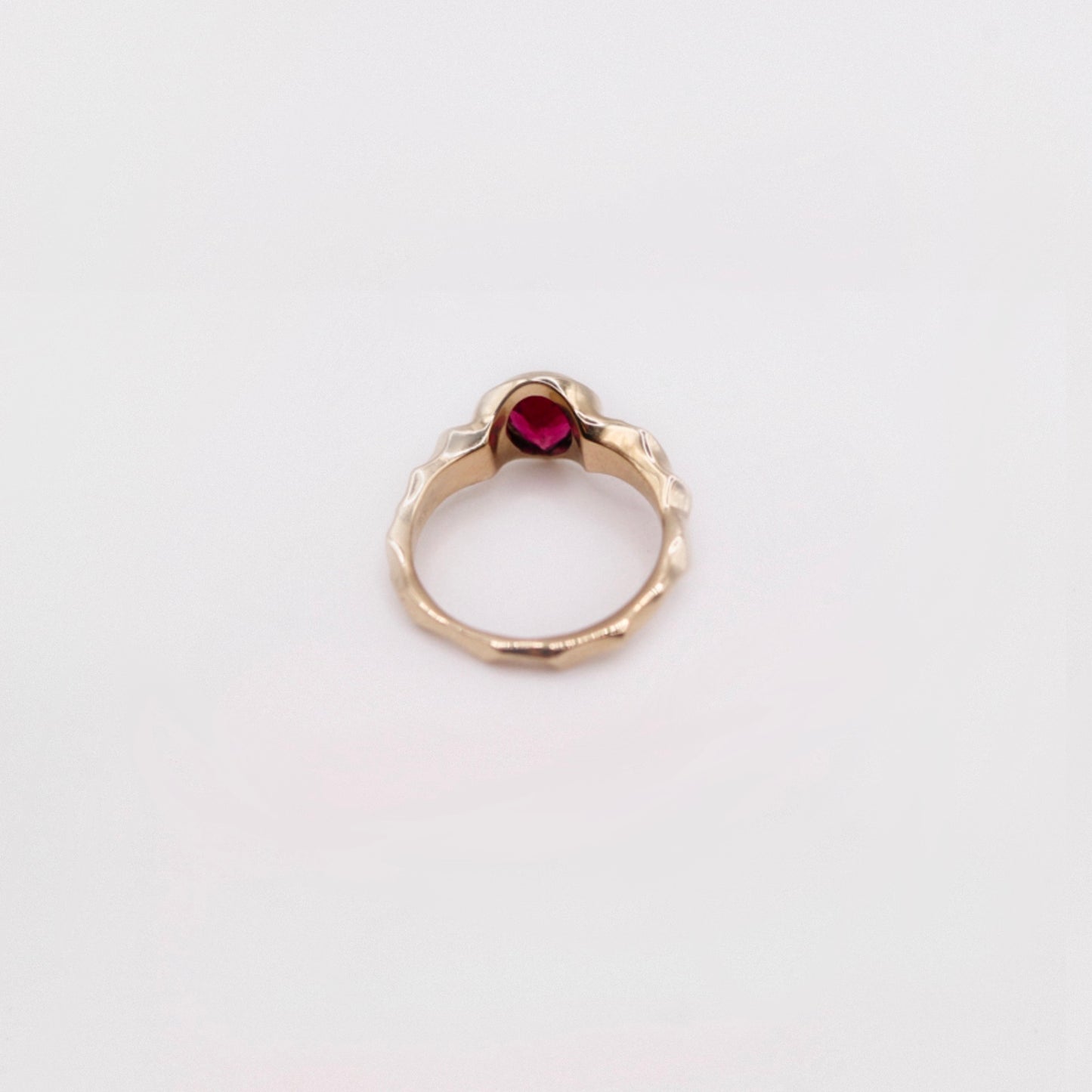 Gold ring with a red gemstone on a light gray background