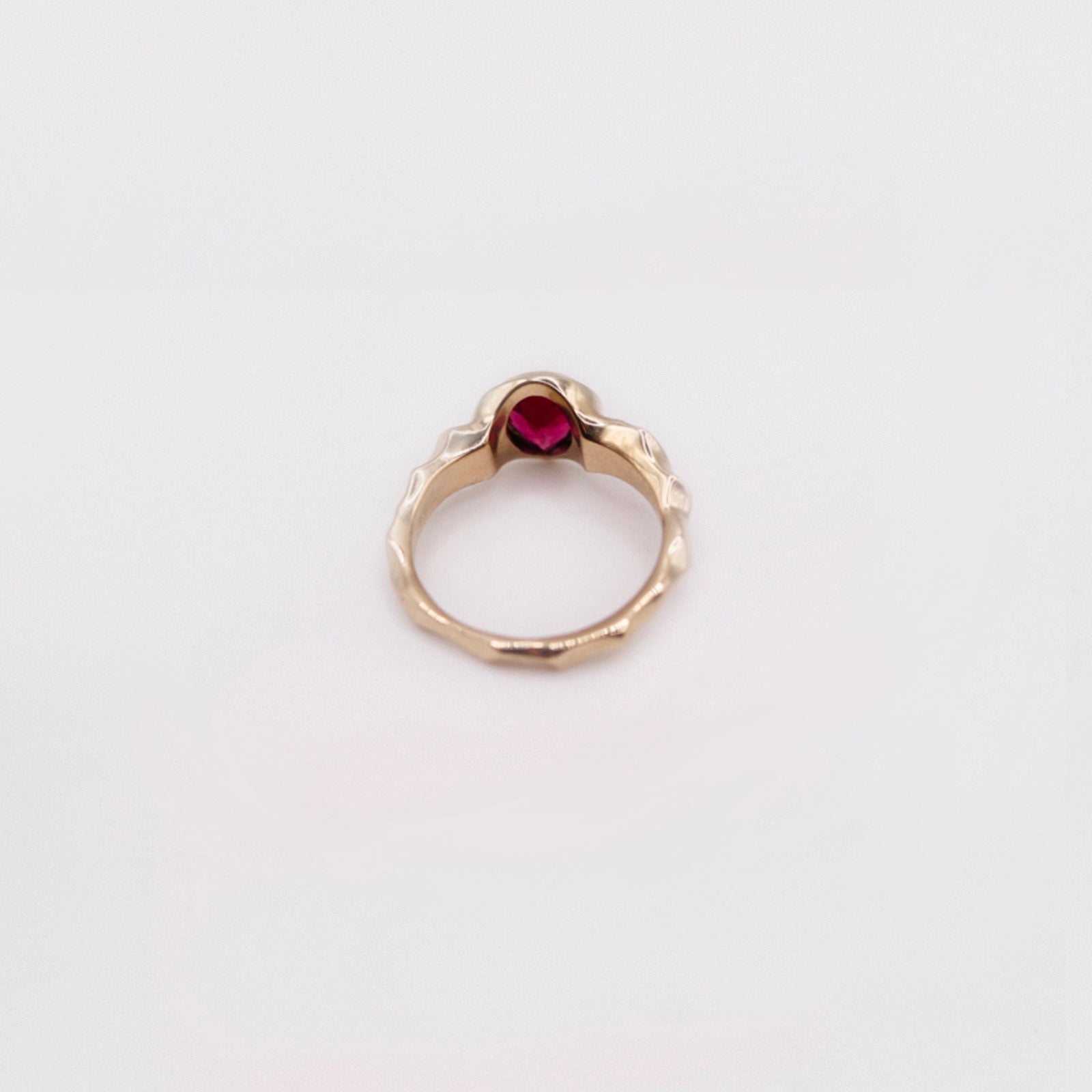 Gold ring with a red gemstone on a light gray background