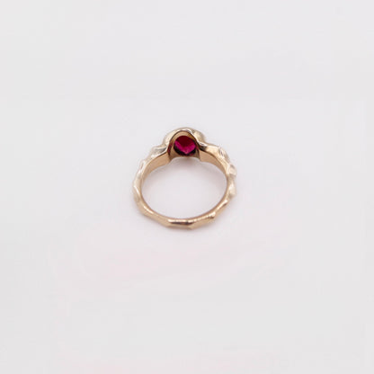 Gold ring with a red gemstone on a light gray background