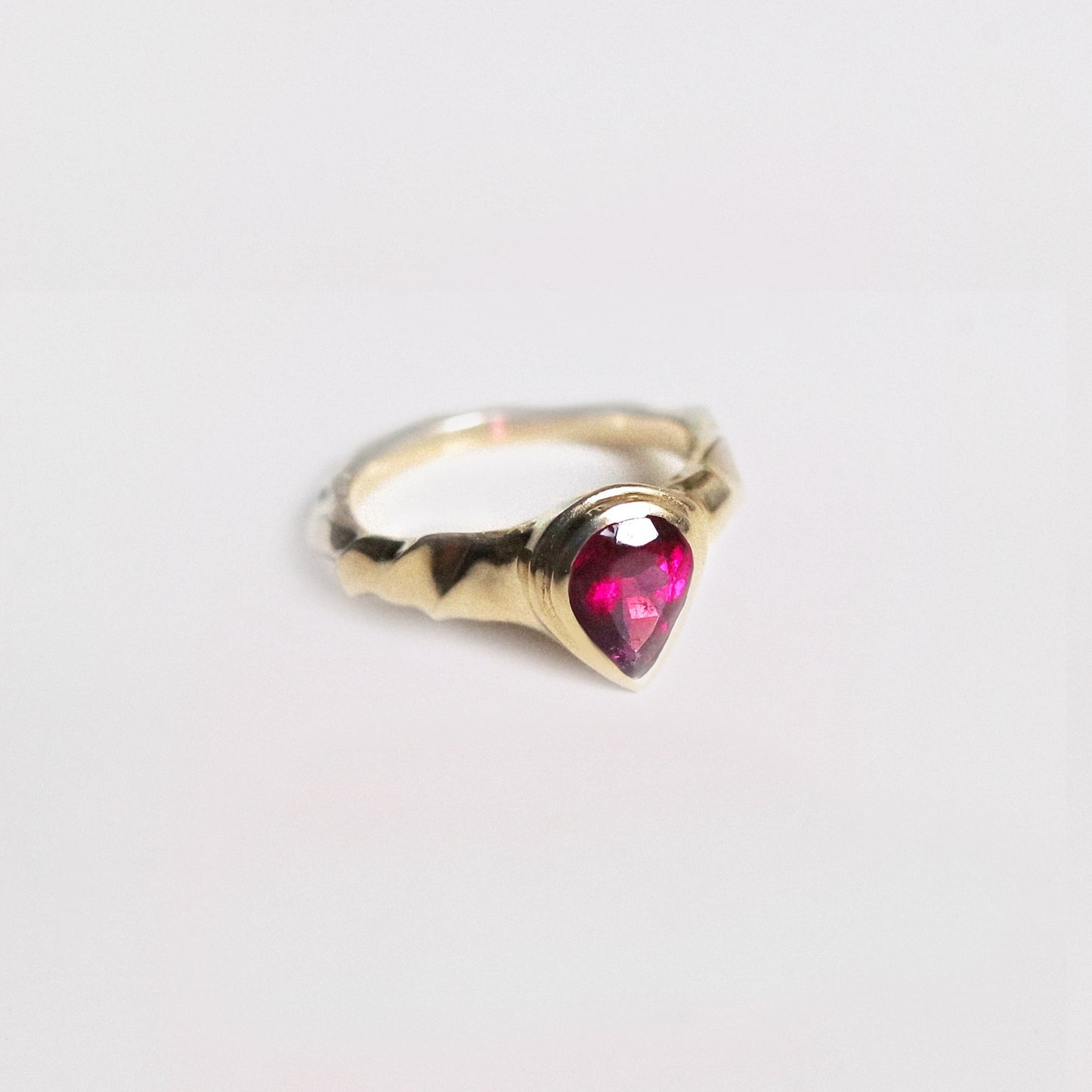 Gold ring with a heart-shaped pink gemstone on a light gray background