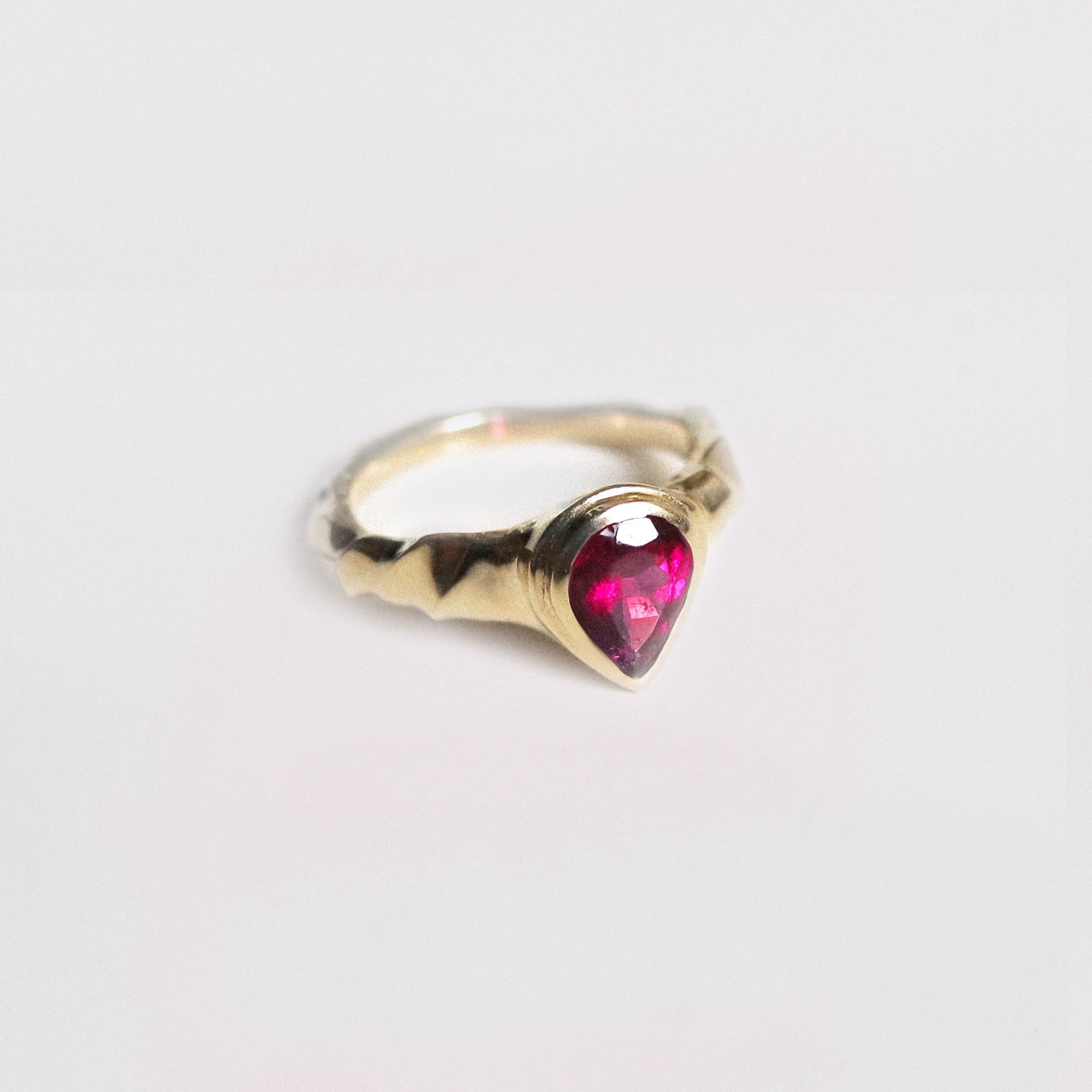 Gold ring with a heart-shaped pink gemstone on a light gray background