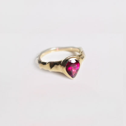 Gold ring with a heart-shaped pink gemstone on a light gray background