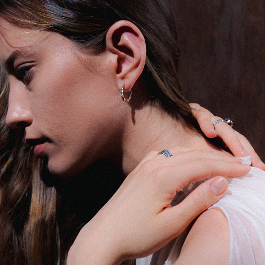 Close-up of a woman wearing a gold hoop earring and a ring on her finger.