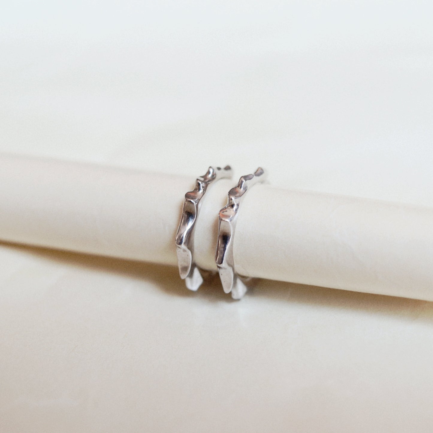 Two small metallic rings with a jagged, thorny edge design, displayed on a textured white paper background.
