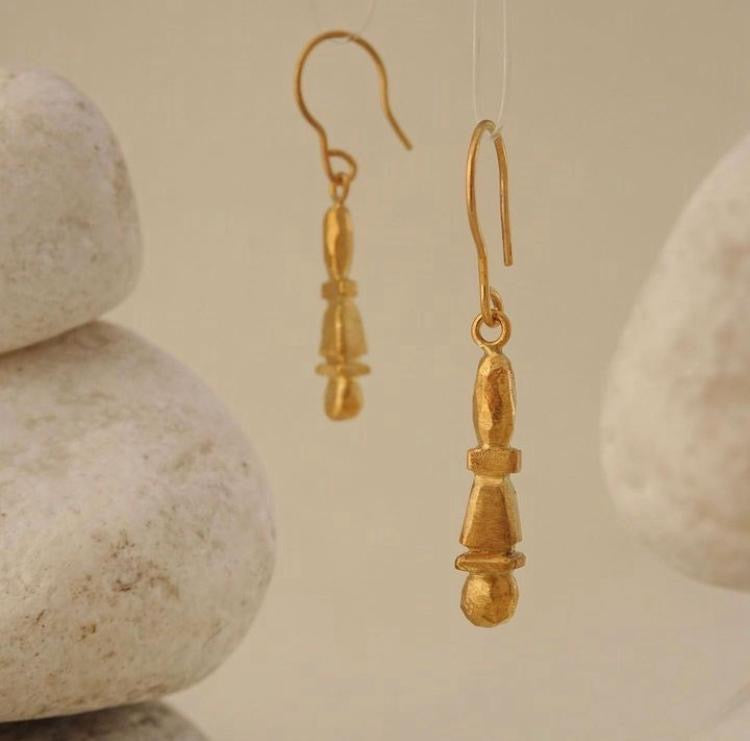 Gold earrings hanging against a beige background with stones.