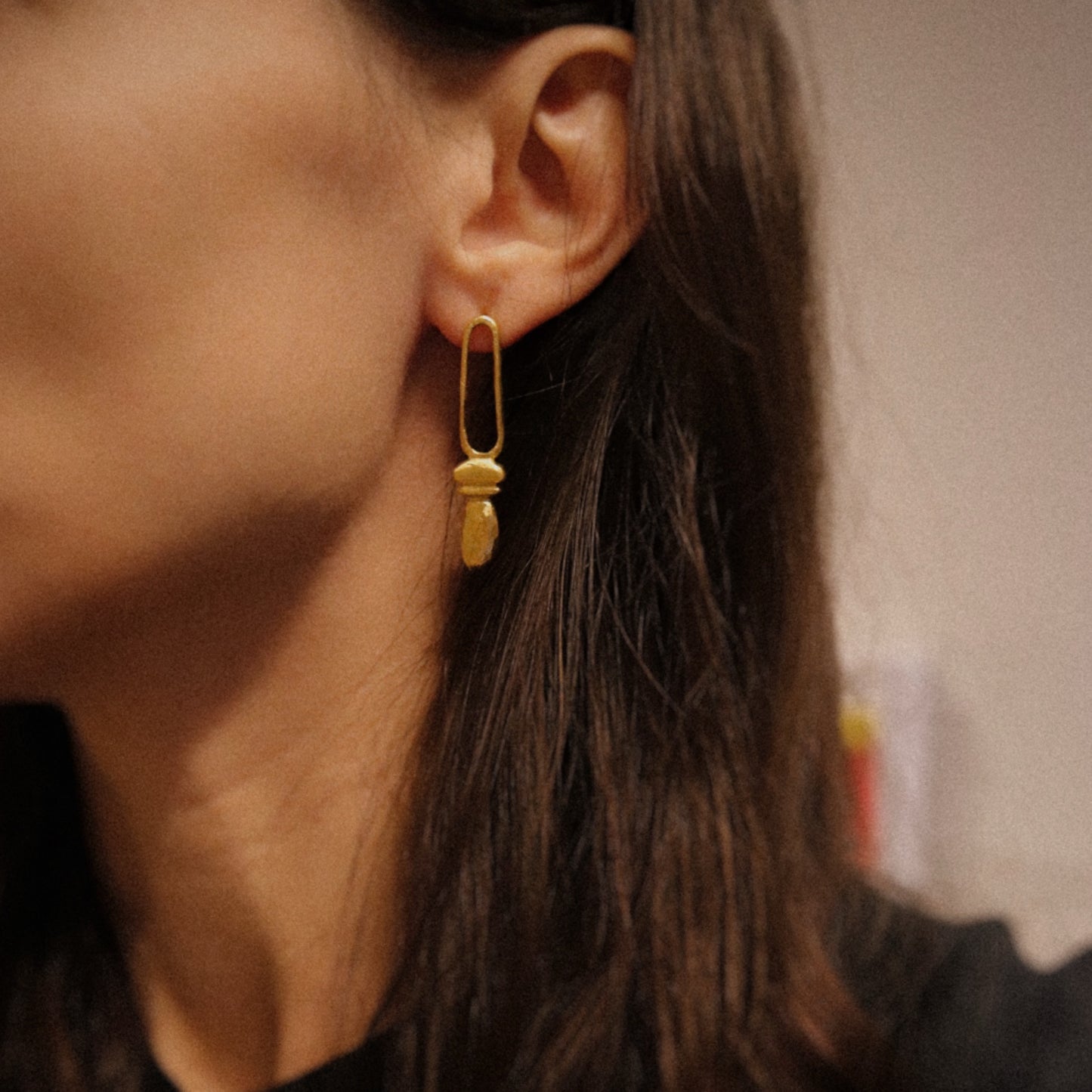 Close-up of a person wearing a gold earring with a blurred background