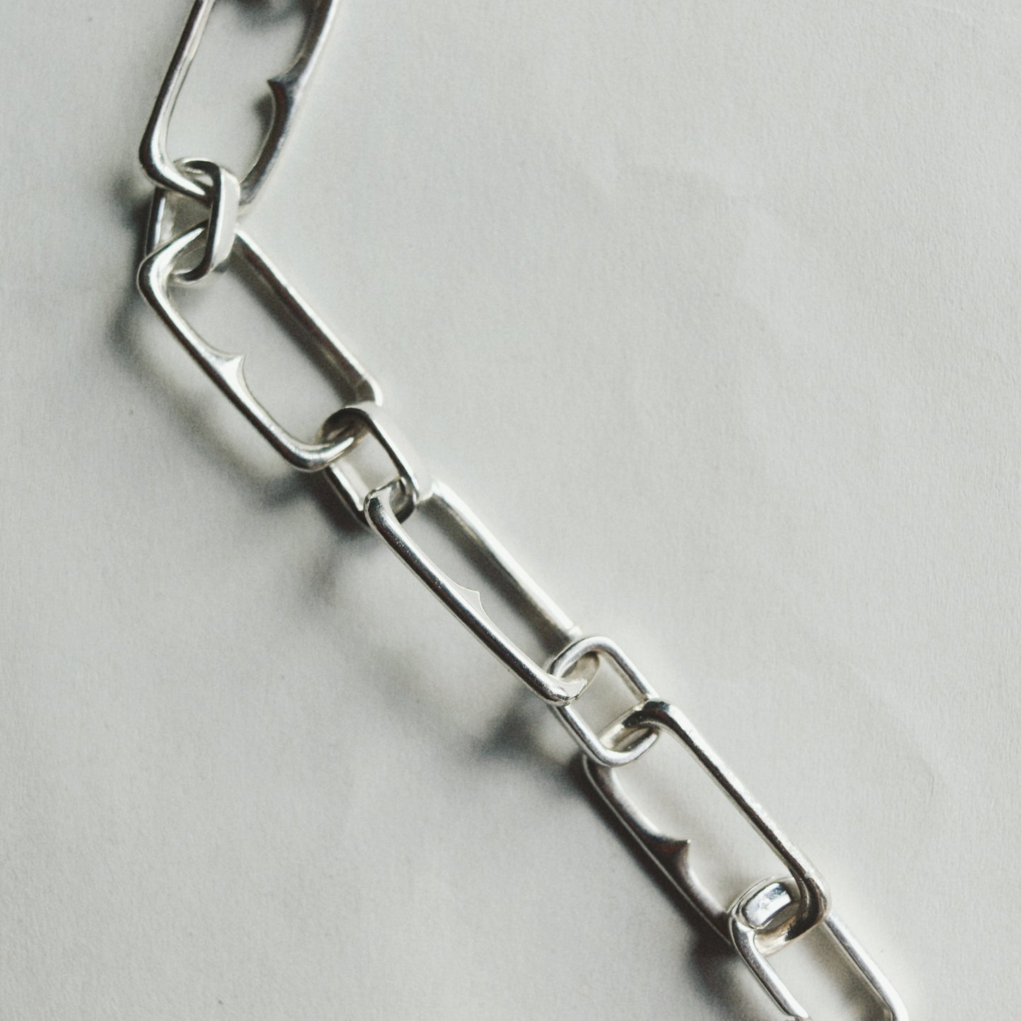 A close-up of a polished silver metal link chain laid diagonally on a light gray textured surface.