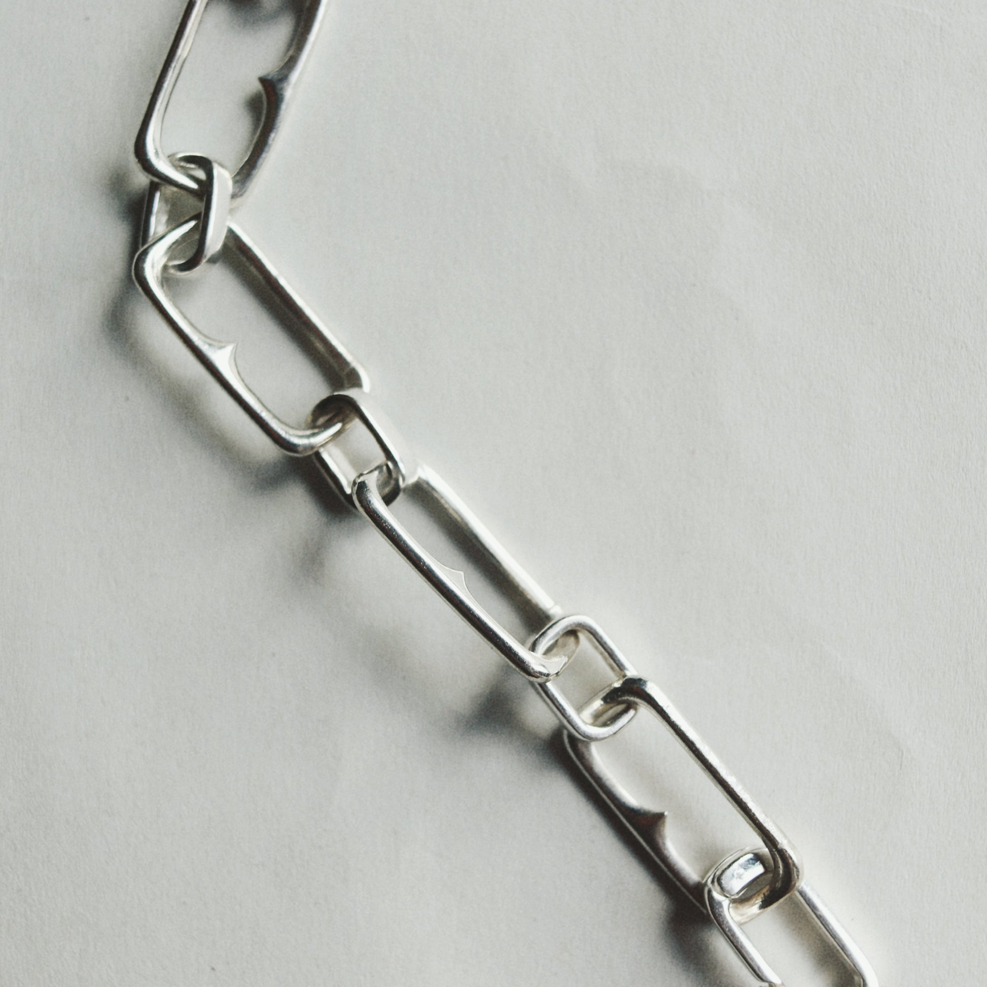 A close-up of a polished silver metal link chain laid diagonally on a light gray textured surface.