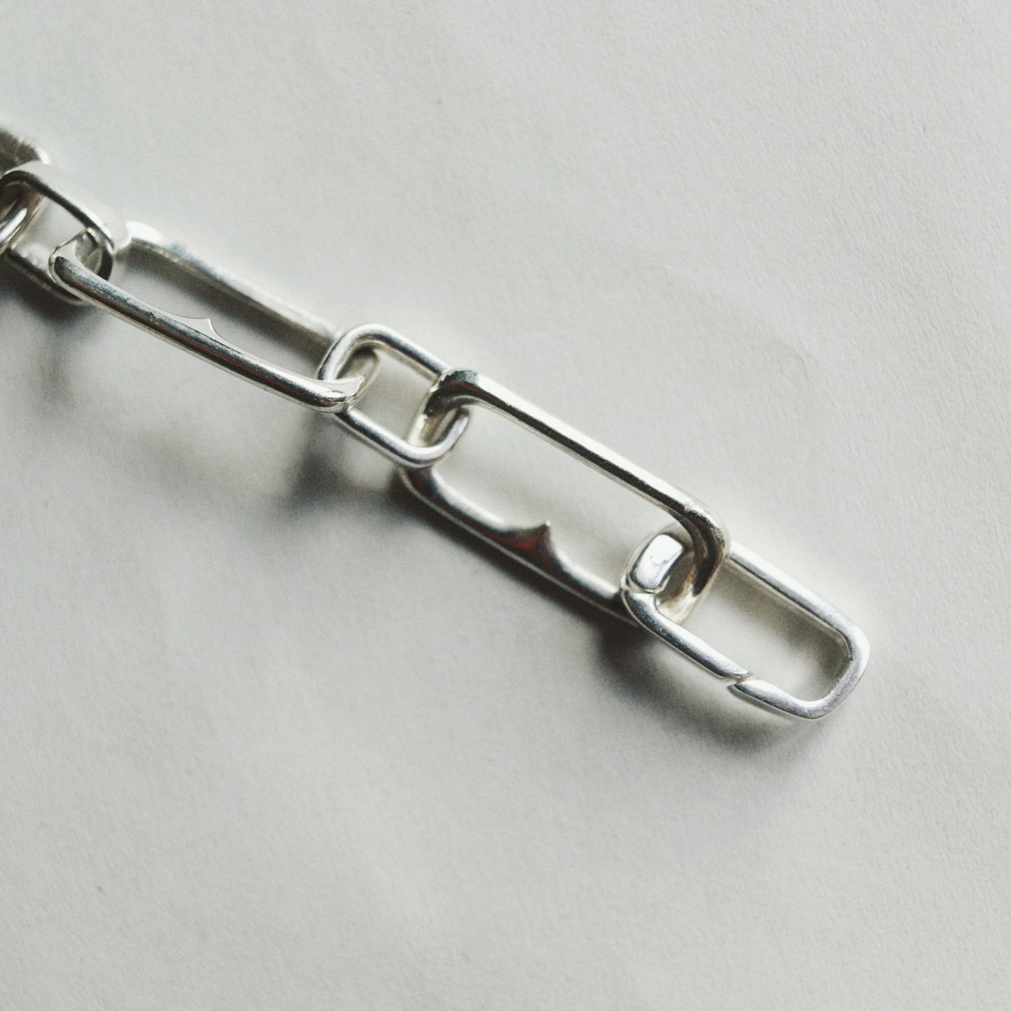 A close-up of a polished silver metal chain with elongated oval links on a light gray background.