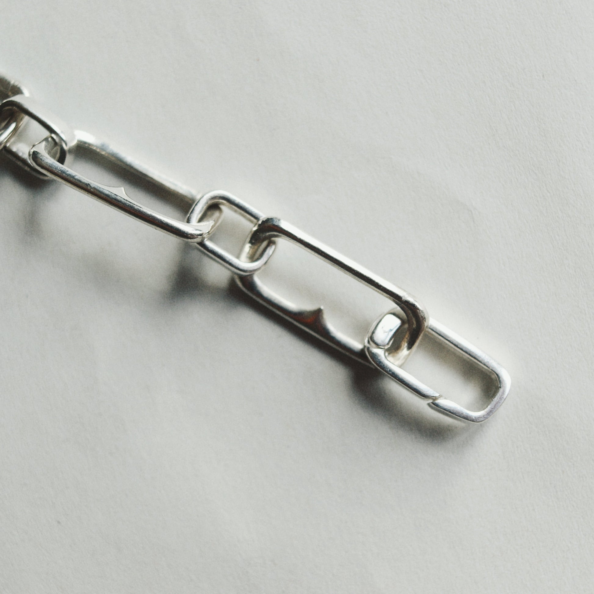 A close-up of a polished silver metal chain with elongated oval links on a light gray background.