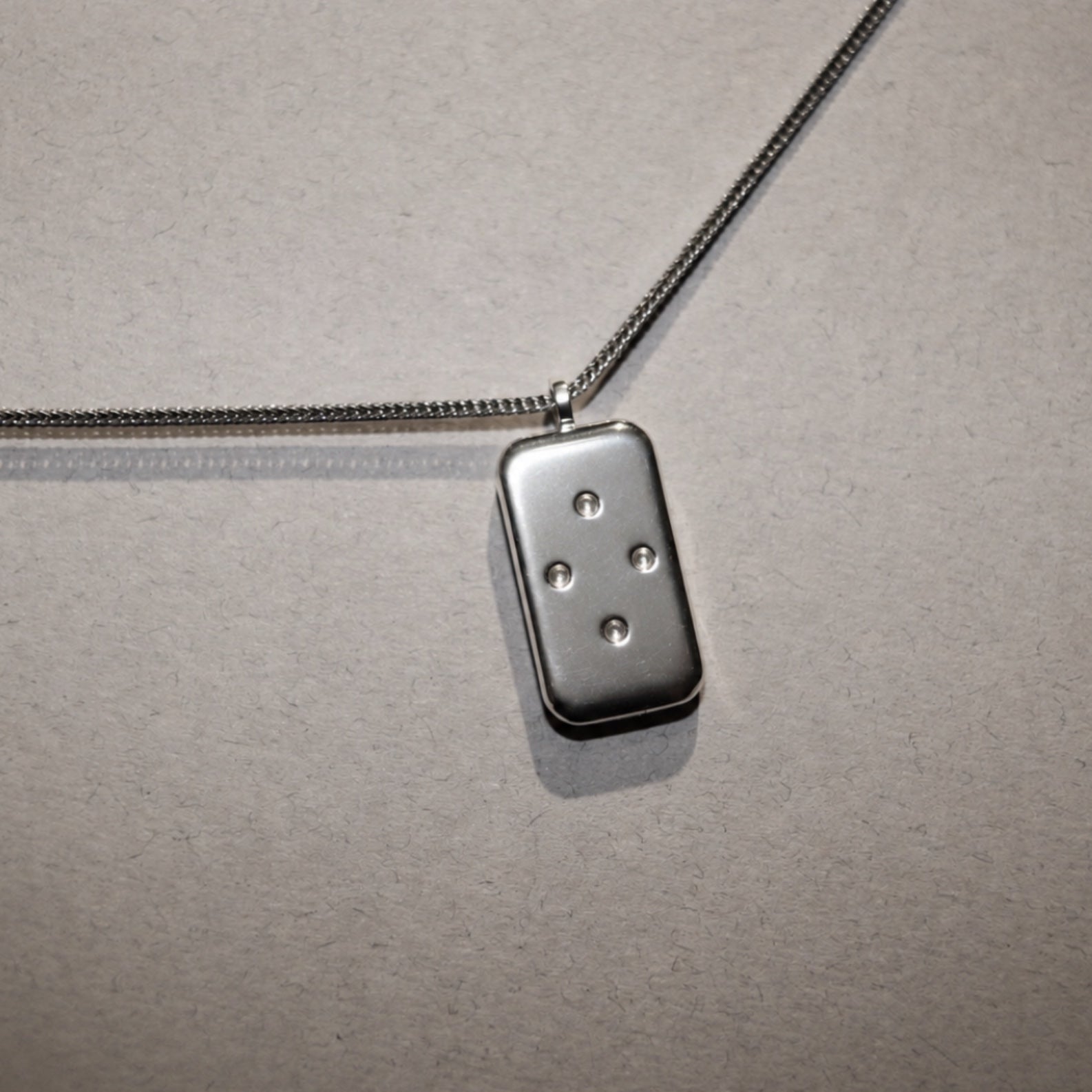 Metallic pendant on a chain against a textured gray background