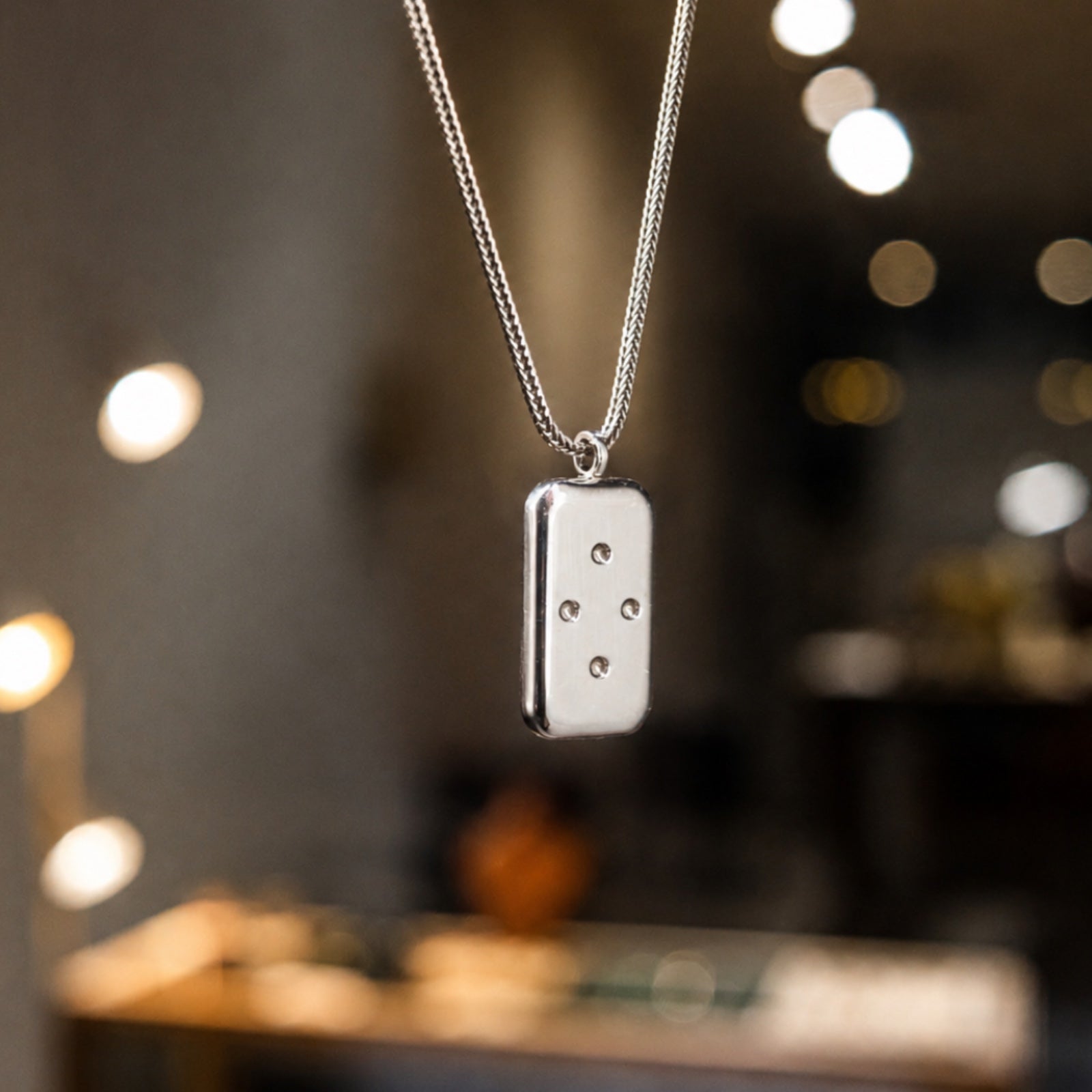Silver necklace with a rectangular pendant against a blurred background
