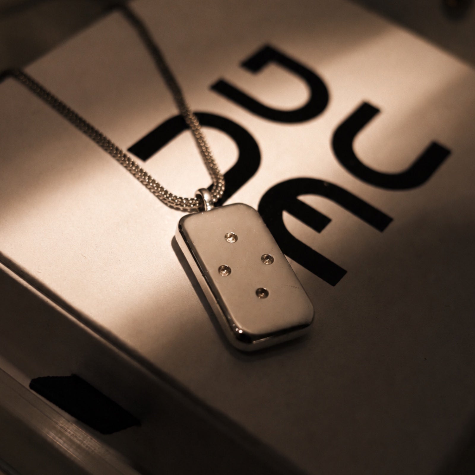Silver pendant necklace on a metallic surface with 'Duc' visible