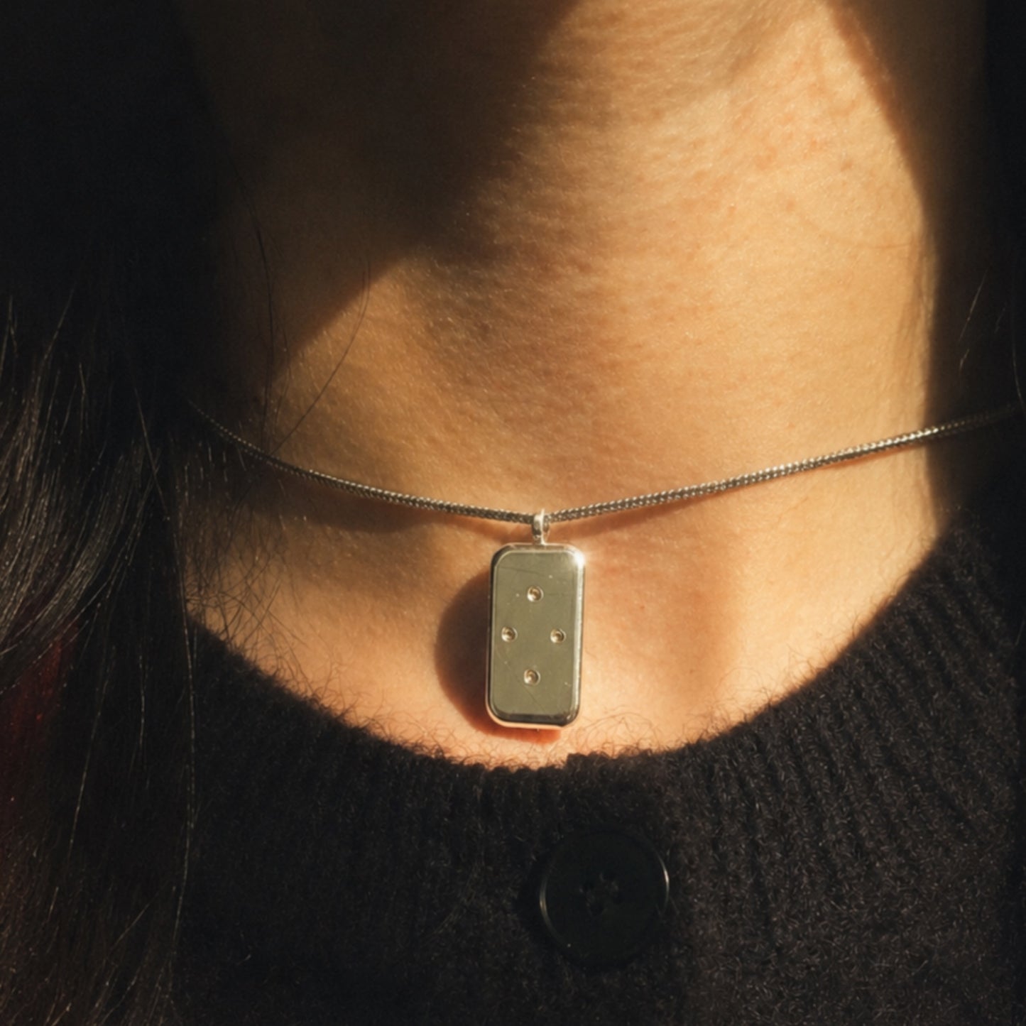 Necklace with a rectangular pendant worn by a person against a dark background