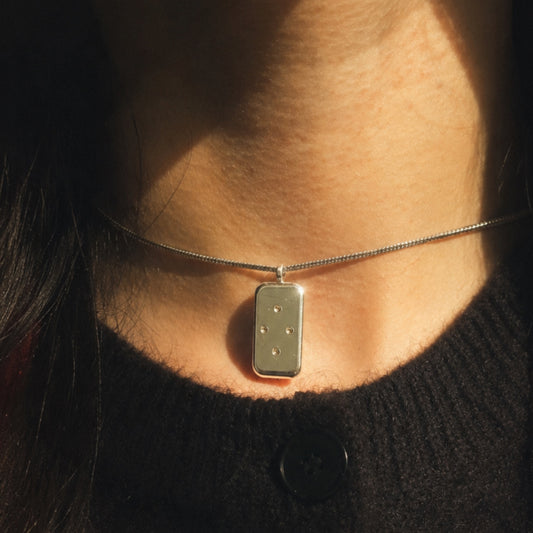 Necklace with a rectangular pendant worn by a person against a dark background