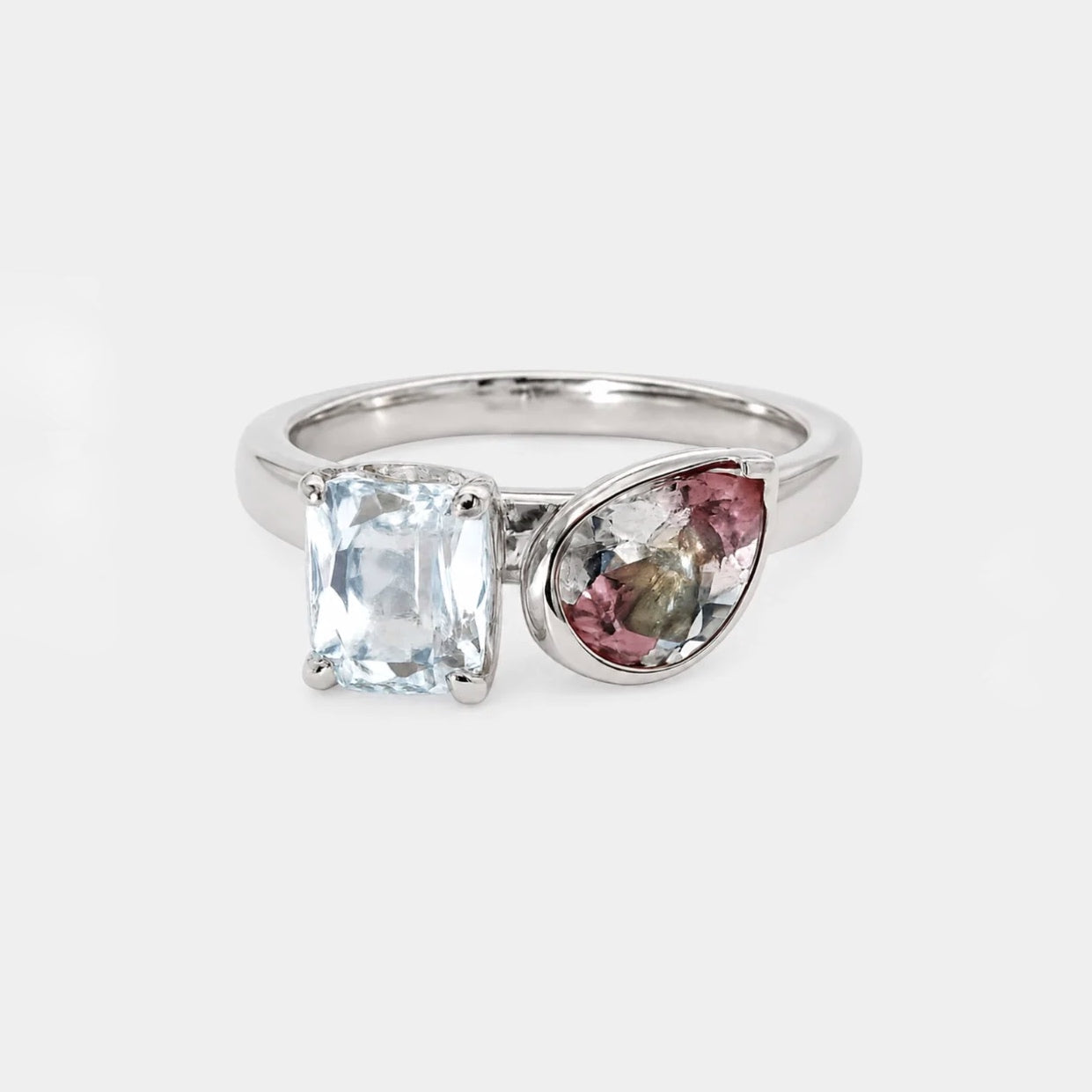 A silver ring featuring a rectangular clear gemstone and a teardrop-shaped multicolor gemstone cluster, set against a light gray background.