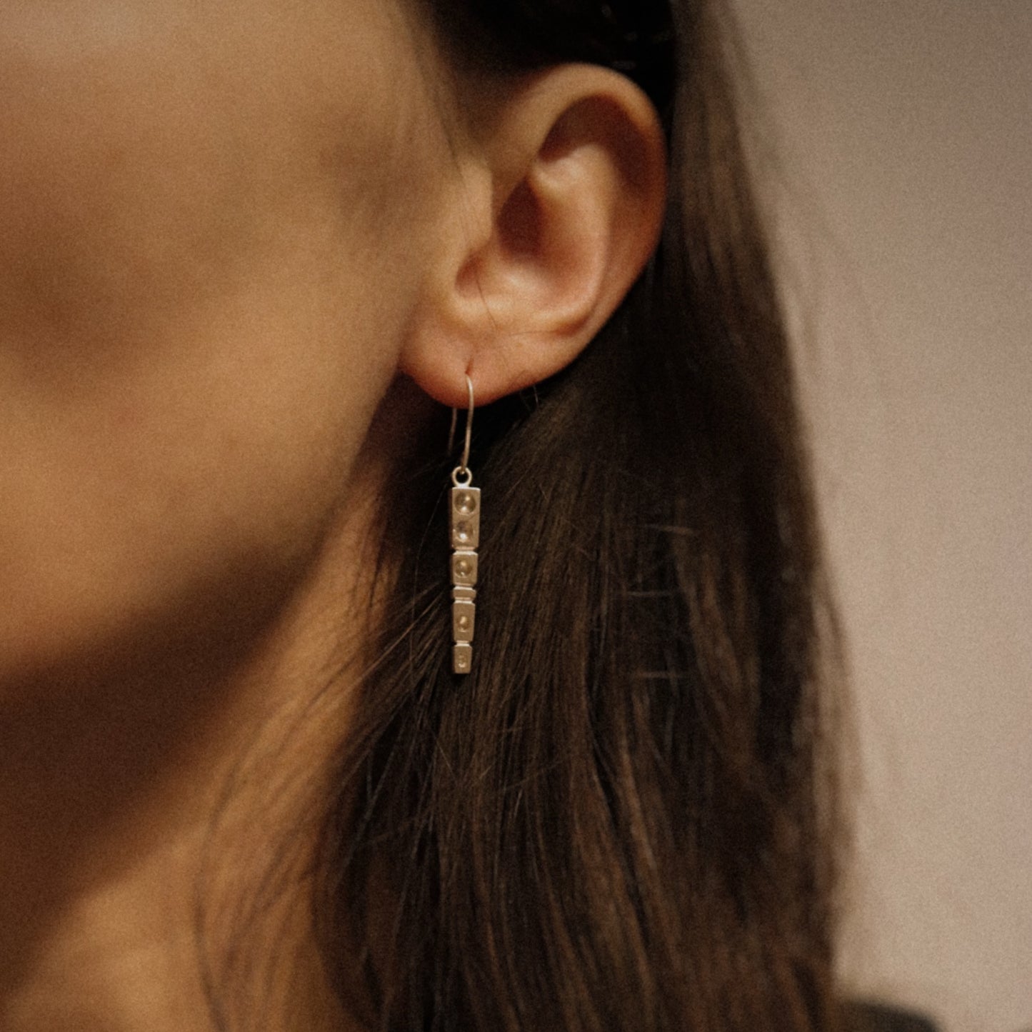 Close-up of an ear wearing a dangling earring with a neutral background