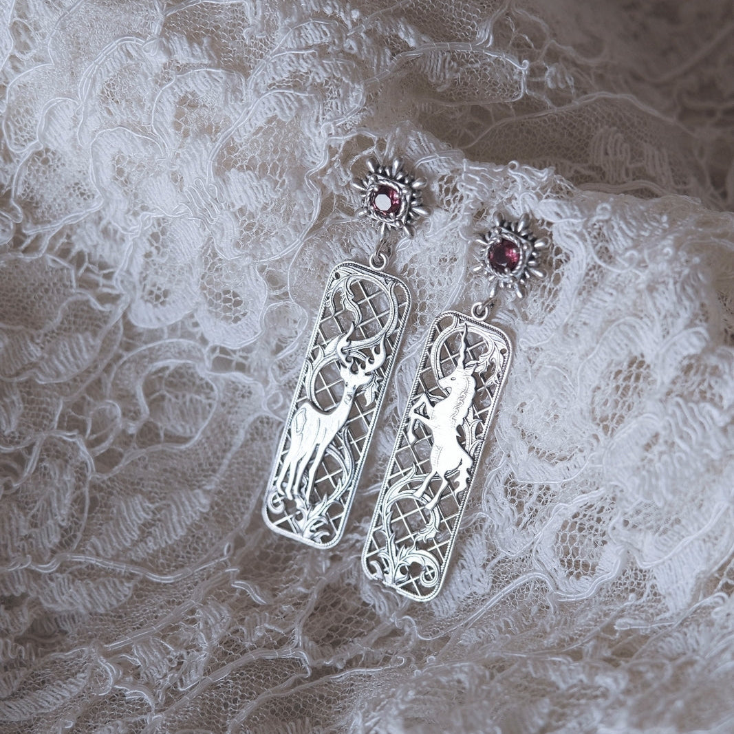 Silver earrings with intricate designs on a lace fabric background