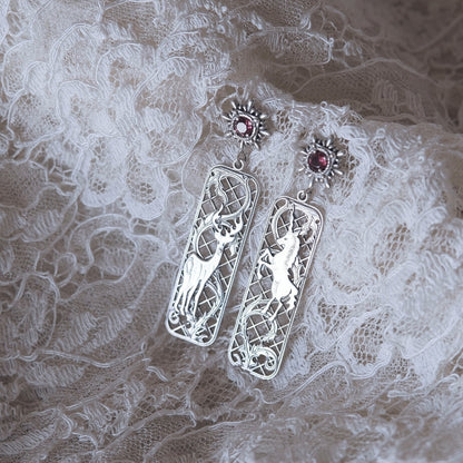 Silver earrings with intricate designs on a lace fabric background