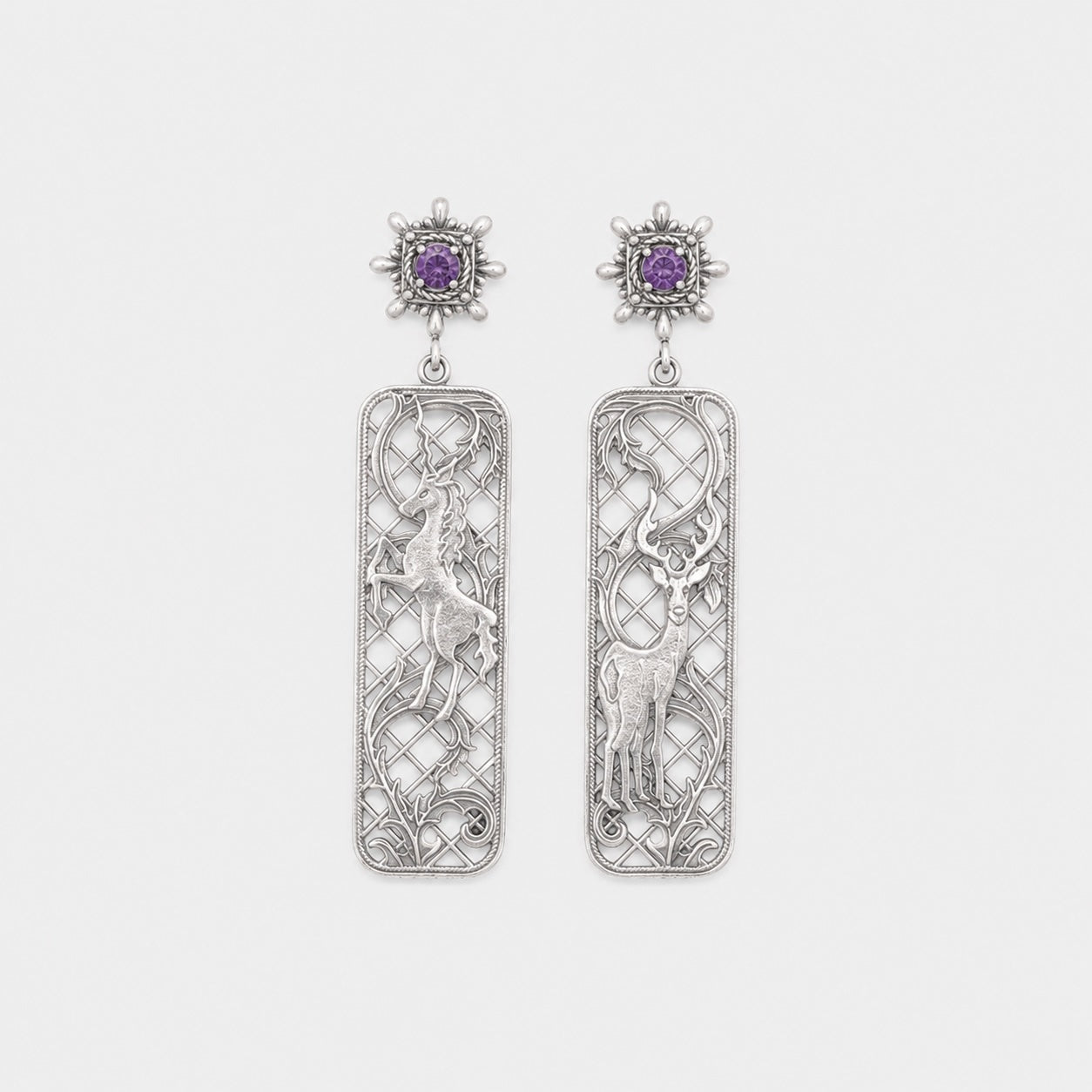 Pair of silver earrings with intricate designs and purple gemstones on a light gray background