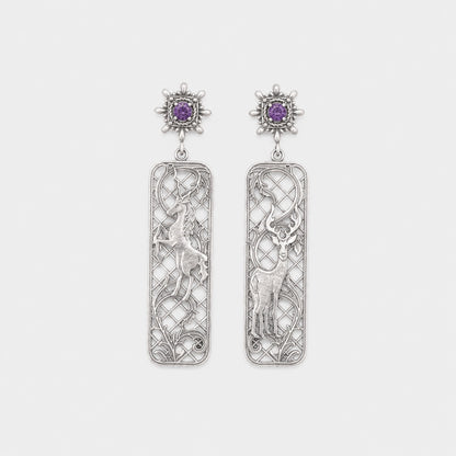 Pair of silver earrings with intricate designs and purple gemstones on a light gray background