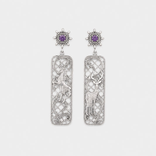 Pair of silver earrings with intricate designs and purple gemstones on a light gray background