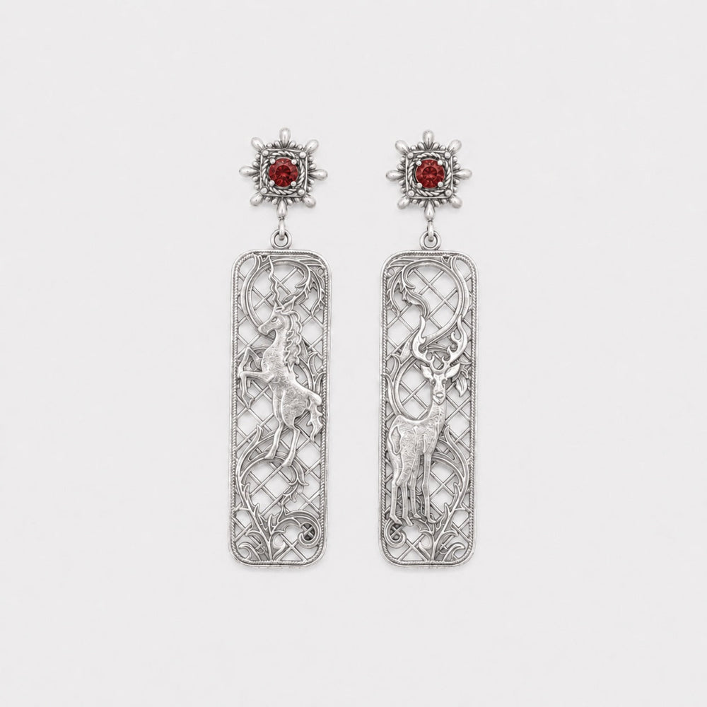 Pair of silver earrings with intricate designs and red gemstones on a white background