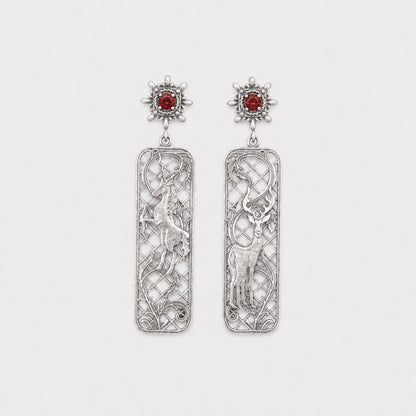 Pair of silver earrings with intricate designs and red gemstones on a white background