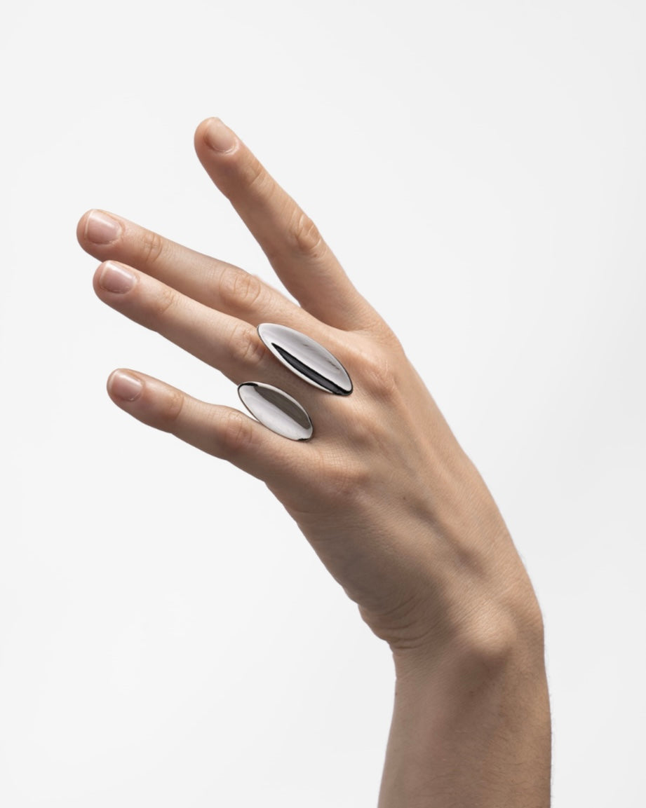 Hand wearing two silver rings on a light gray background