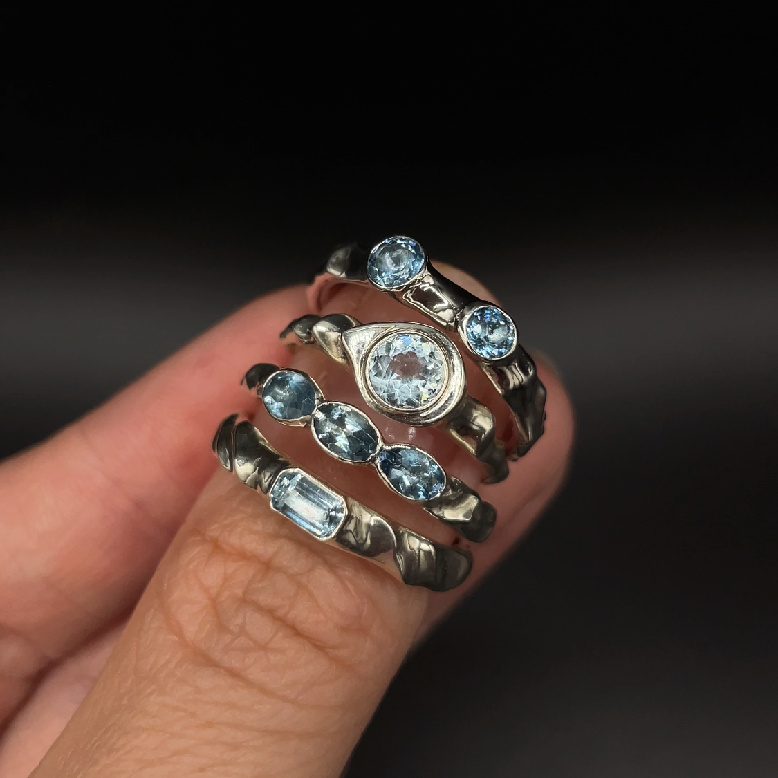Stack of silver rings with gemstones on a finger against a dark background