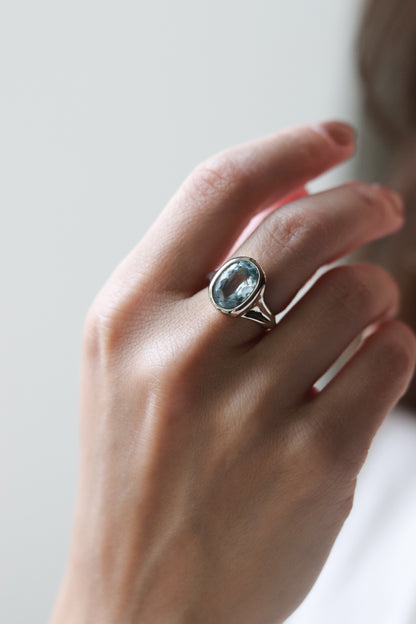 Hand wearing a ring with a blue gemstone on a neutral background