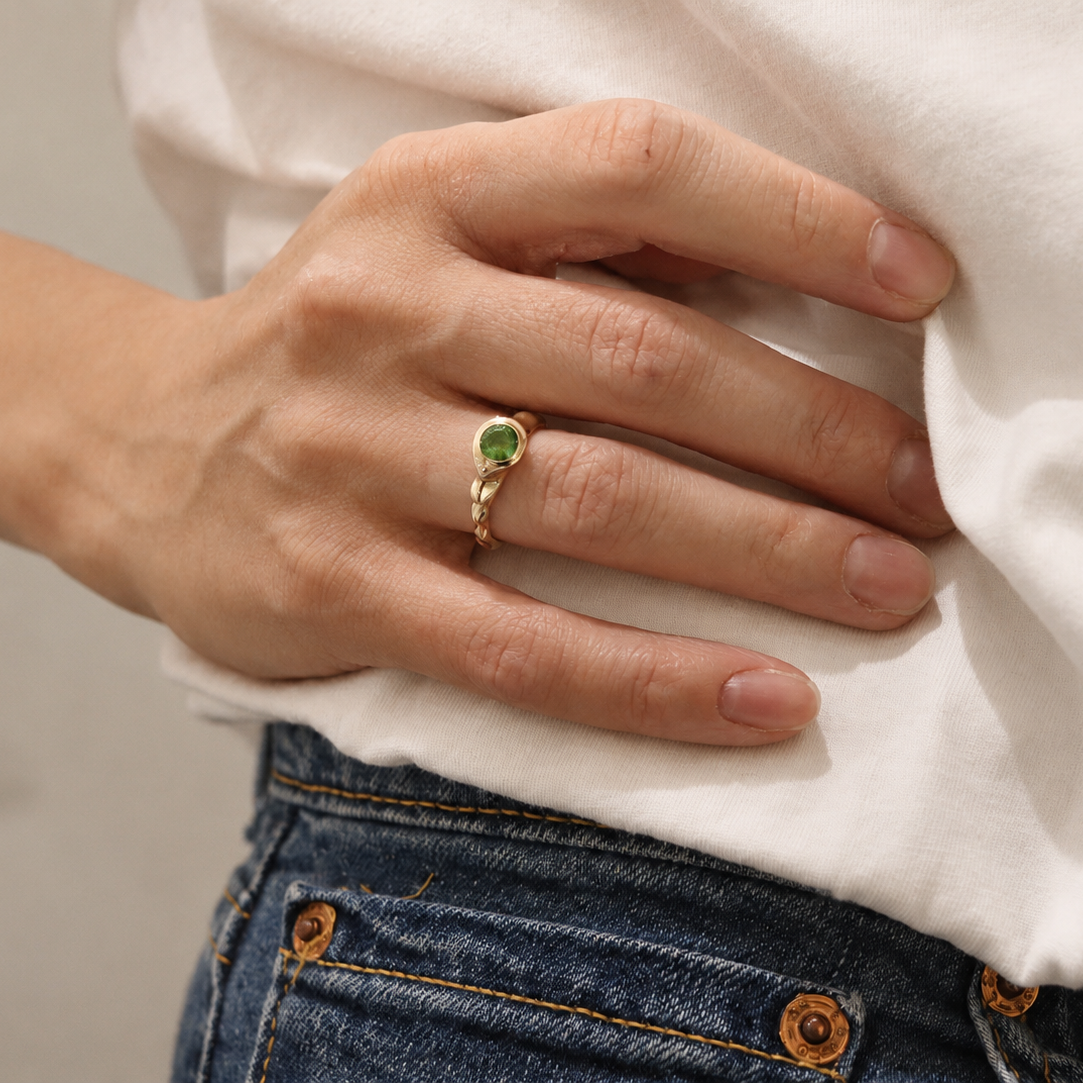 Person wearing a gold ring with a green gemstone on a plain background