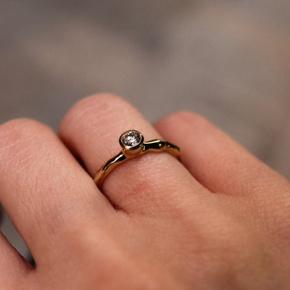 Gold ring with a diamond on a person's finger against a blurred background