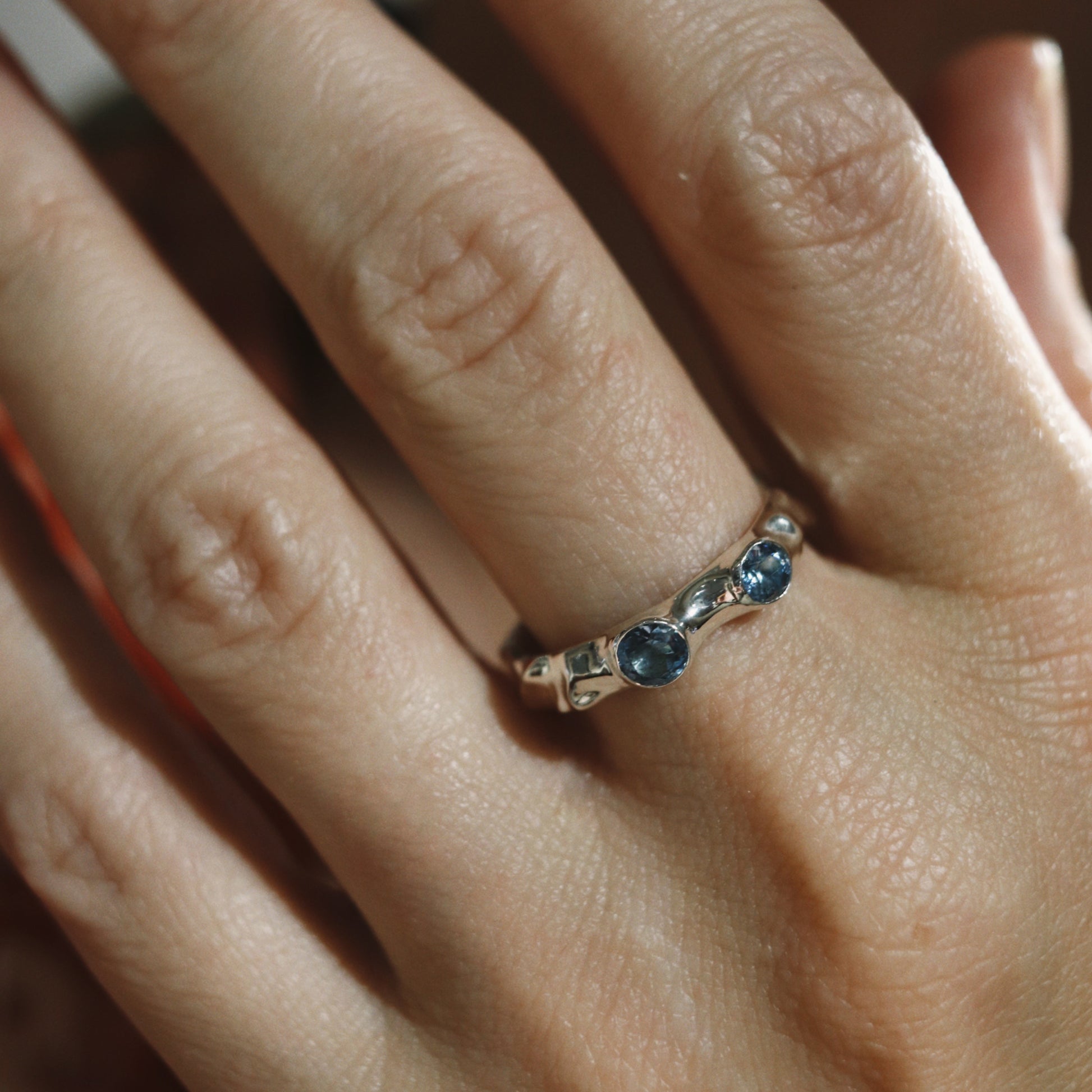 Close-up of a hand wearing a ring with blue gemstones on a blurred background