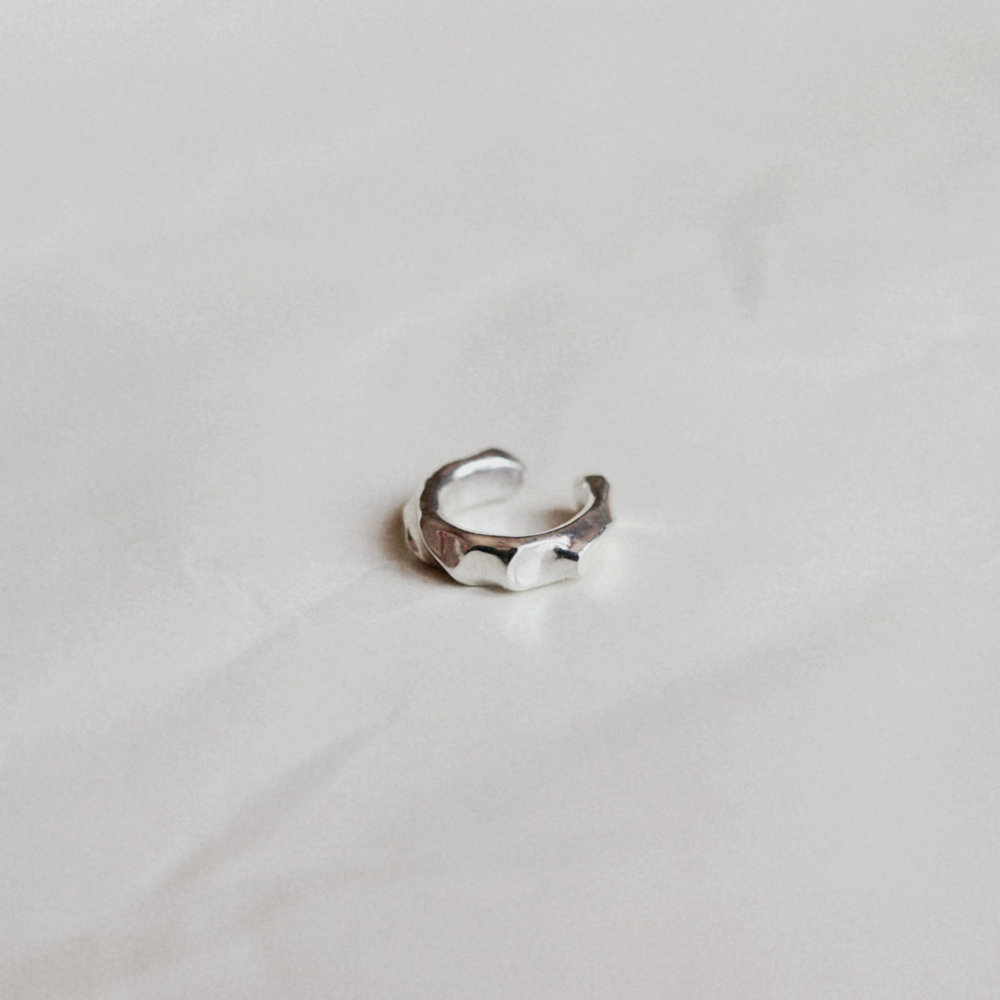 A silver open-toe ring with a hammered, textured finish, resting on a light gray marble surface.
